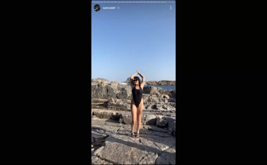Sophoulla in black swimsuit on rocky beach.