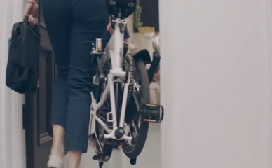 Jane Douglas wearing pants walking with folded bike.